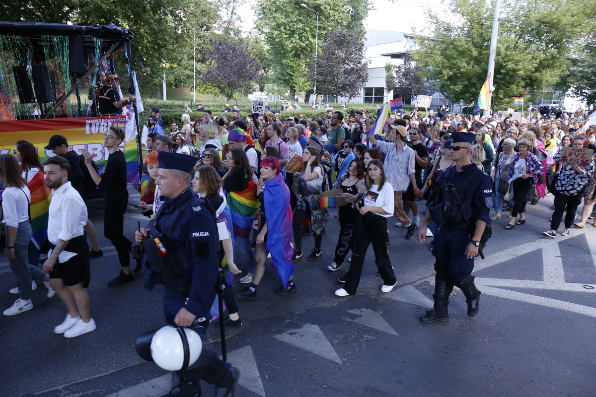 Zdjęcie przedstawia przemarsz uczestników marszu równości. W pierwszym planie policjanci dbający o bezpieczeństwo.