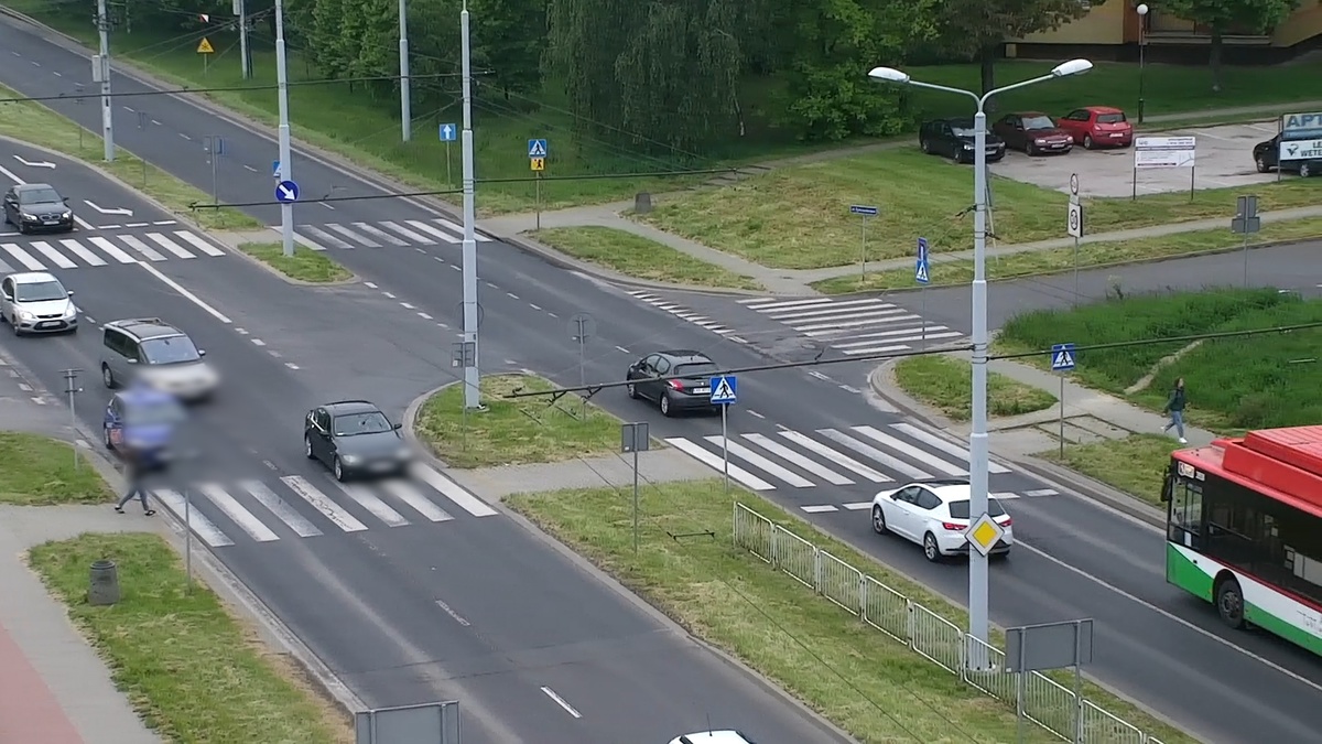 Ujęcie z drona na którym widać kobietę wchodząca na przejście dla pieszych oraz kierowcę pojazdu osobowego który wjeżdża na przejście.