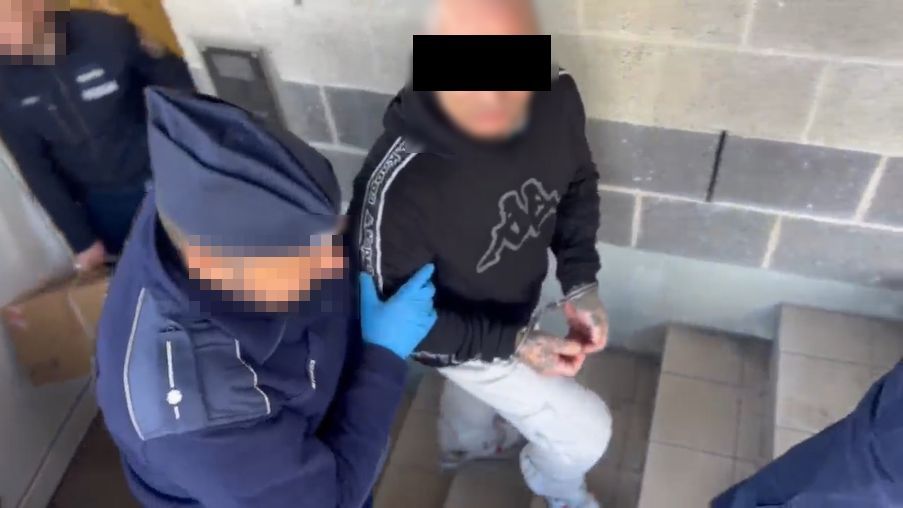 Policjanci prowadzą zatrzymanego mężczyznę.