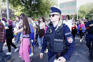 Po prawej stronie zdjęcia widzimy policjantkę która dba o bezpieczeństwo uczestników marszu równości. W głębi zdjęcia osoby biorące udział w marszu przez Lublin.