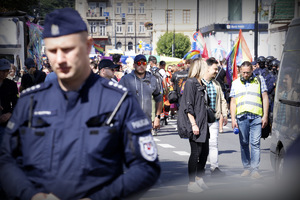 W pierwszym planie zdjęcia umundurowany policjant ubrany w granatowy mundur. W drugim planie uczestnicy marszu równości w Lublinie.