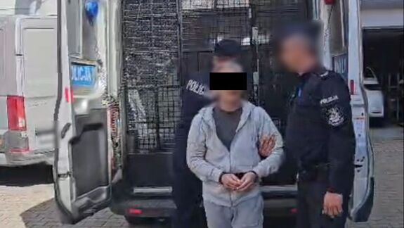 Policjanci prowadzą zatrzymanego mężczyznę.