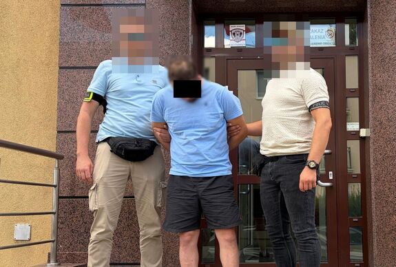Policjanci prowadzą zatrzymanego mężczyznę, który wyłudził od kobiety ponad 110 000 złotych.