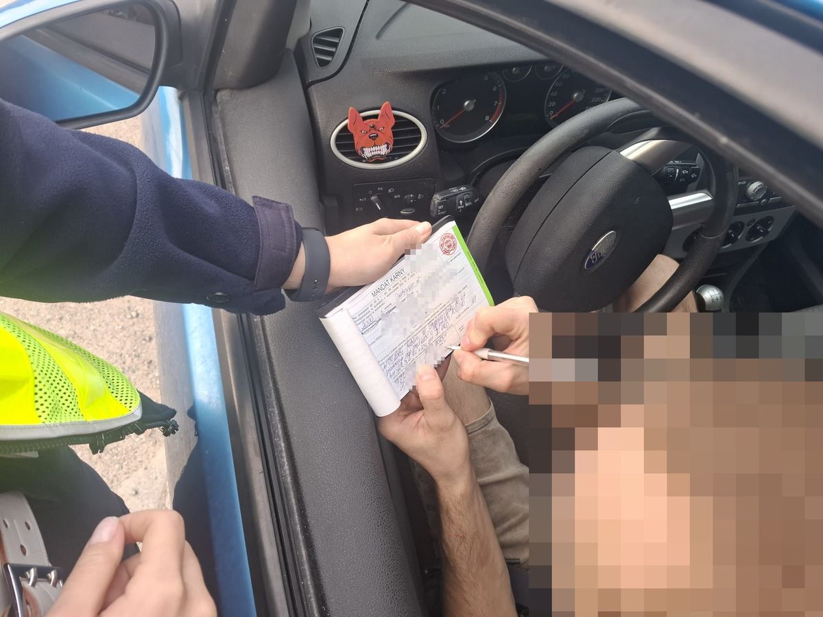 policjant podczas kontroli drogowej, kierowca podpisuje mandat karny