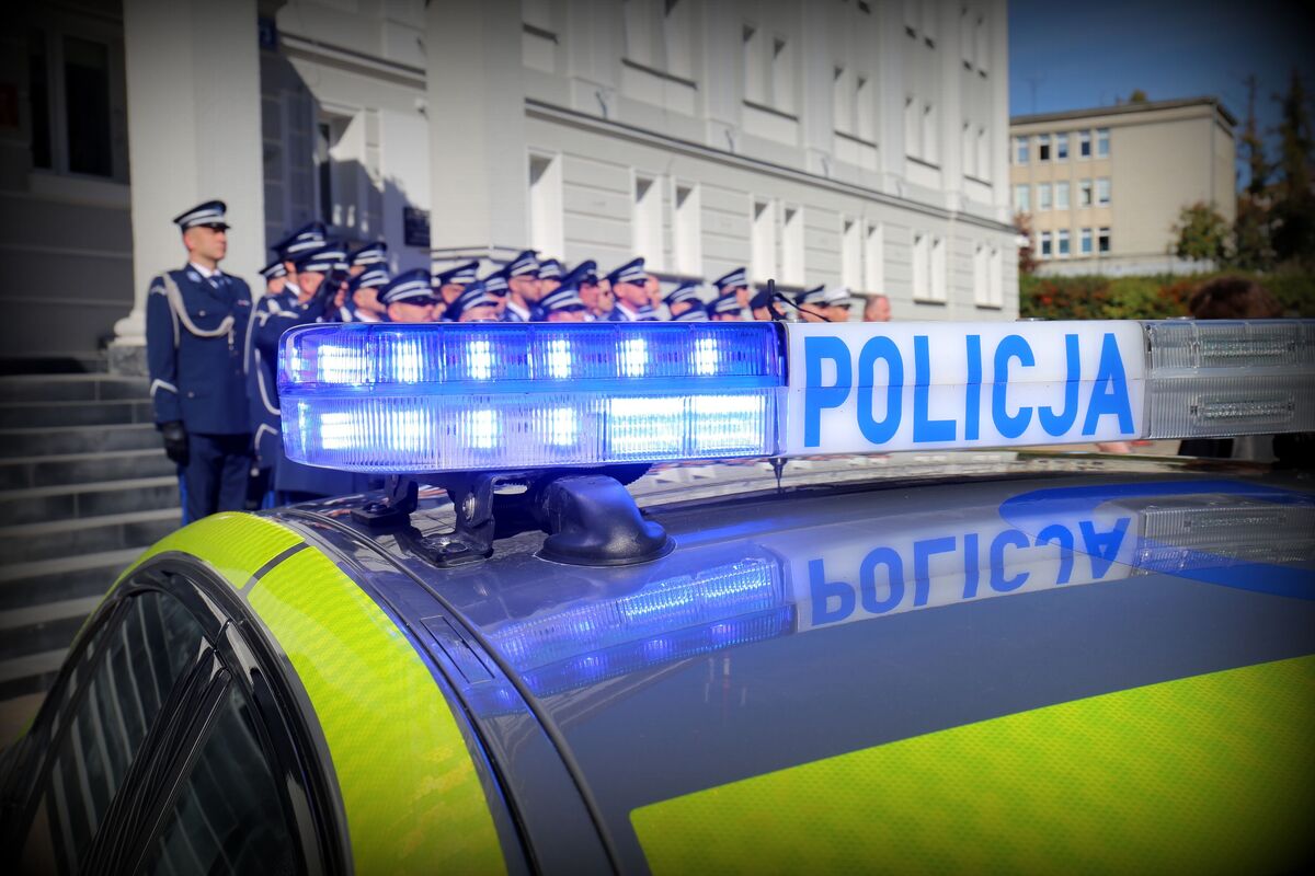 radiowóz, w tle policjanci oddają hołd przed budynkiem komendy Wojewódzkiej Policji w Lublinie