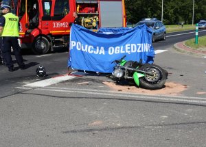 motocykl leżący na skrzyżowaniu, parawan z napisem policja, w tle widać policjanta i wóz strażacki