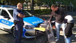 policjant stojący przy radiowozie, uczestnicy oglądają policyjne stoisko