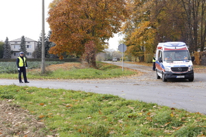 Policjanci kierują ruchem w pobliżu lotniska. Po prawej stronie zdjęcia widzimy karetkę pogotowia z włączonymi sygnałami świetlnymi, która jedzie z poszkodowanym do szpitala.