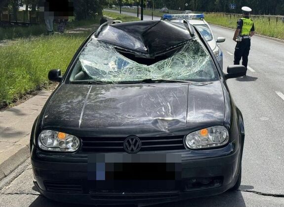 uszkodzony pojazd na drodze, w tle widać radiowóz i policjanta